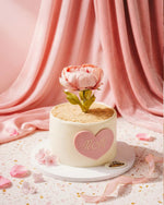 Small cake with a pink flower and 'mom' heart on a pink fabric background