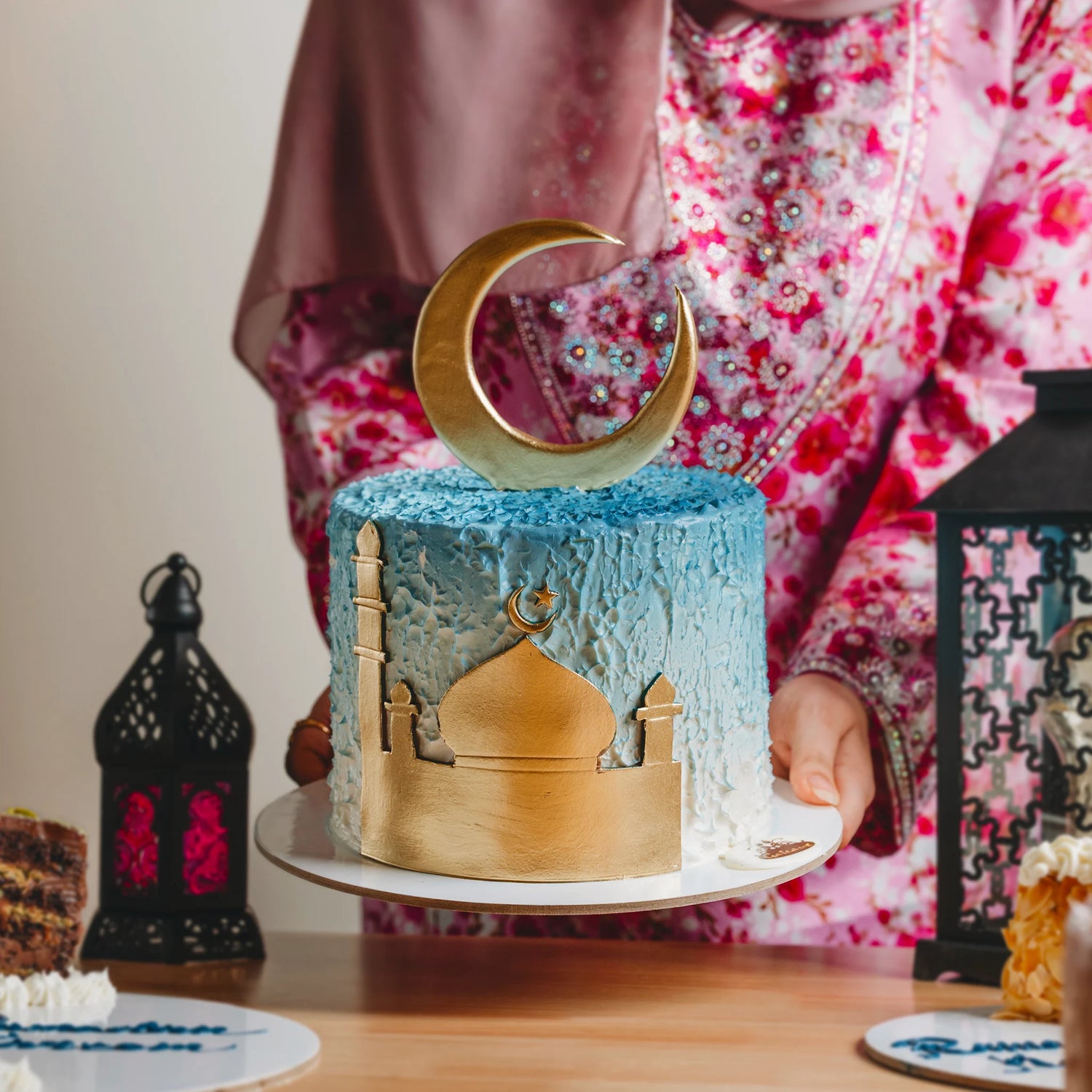 Decorative cake with a crescent moon and mosque silhouette on a table.