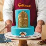 Turquoise cake with gold door design held by a person wearing a 'Gateaux' apron.
