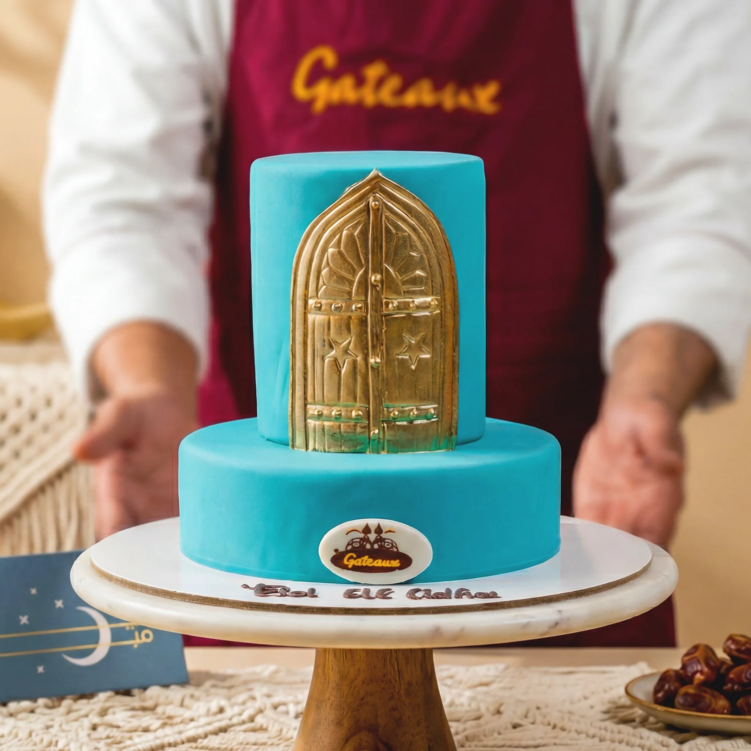 Turquoise cake with gold door design held by a person wearing a 'Gateaux' apron.