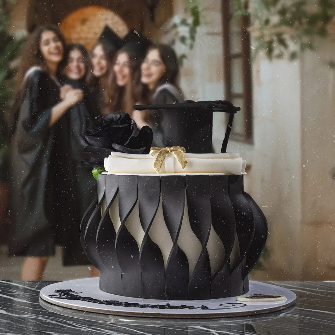 Graduation-themed cake with black cap and tassel on a blurred background of graduates.