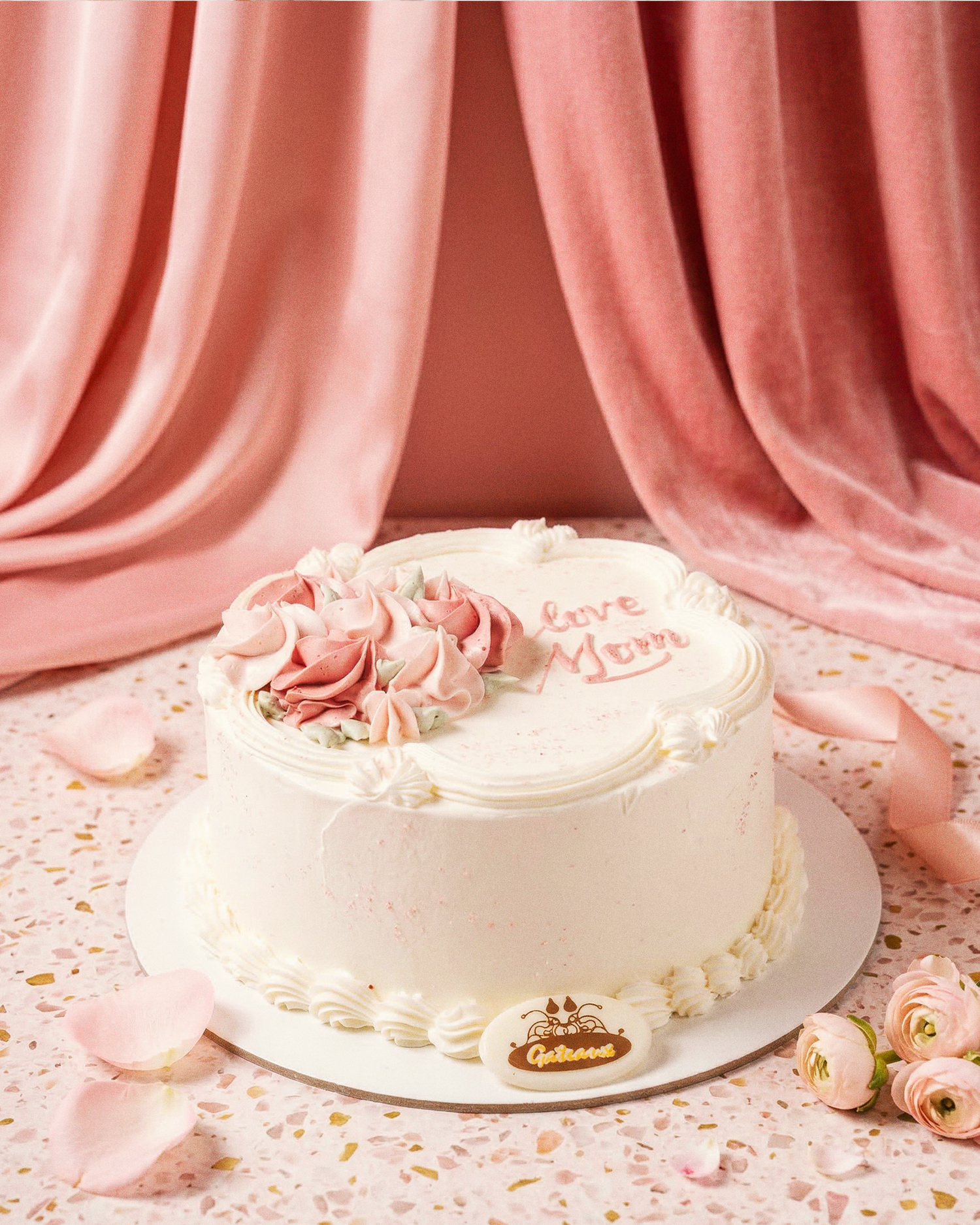 White cake with pink flowers and 'Love Mom' text on a pink background