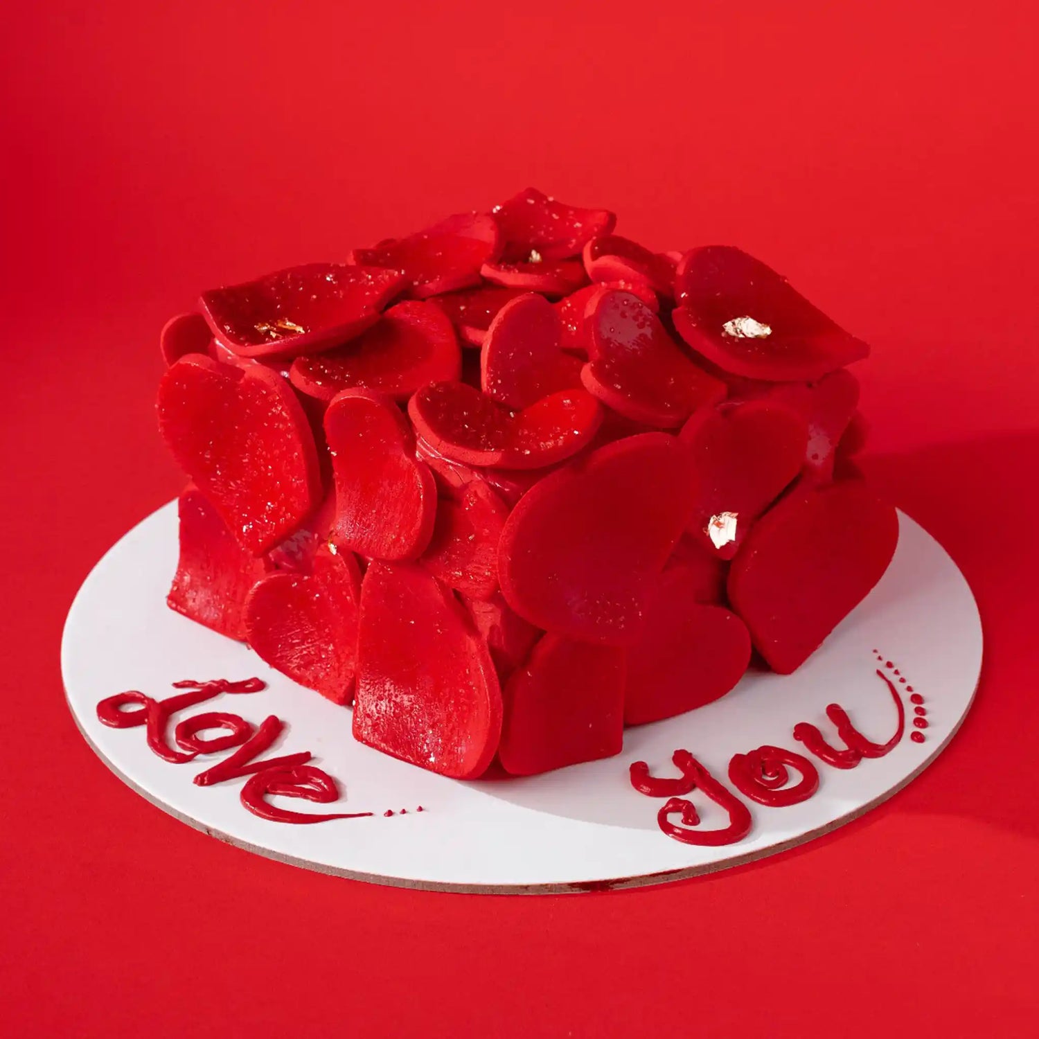 Red cake with rose petals on a white plate against a red background