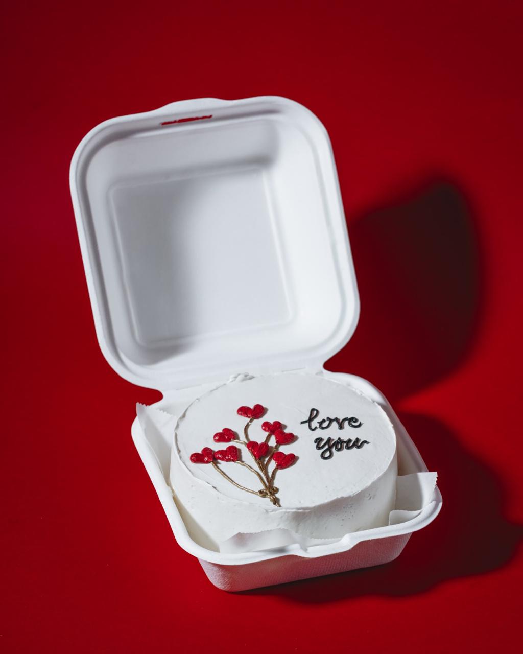 Small cake with 'love you' message in a takeout container on a red background
