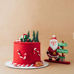 Red Christmas cake with candy cane decorations and a Santa Claus figurine on a beige background
