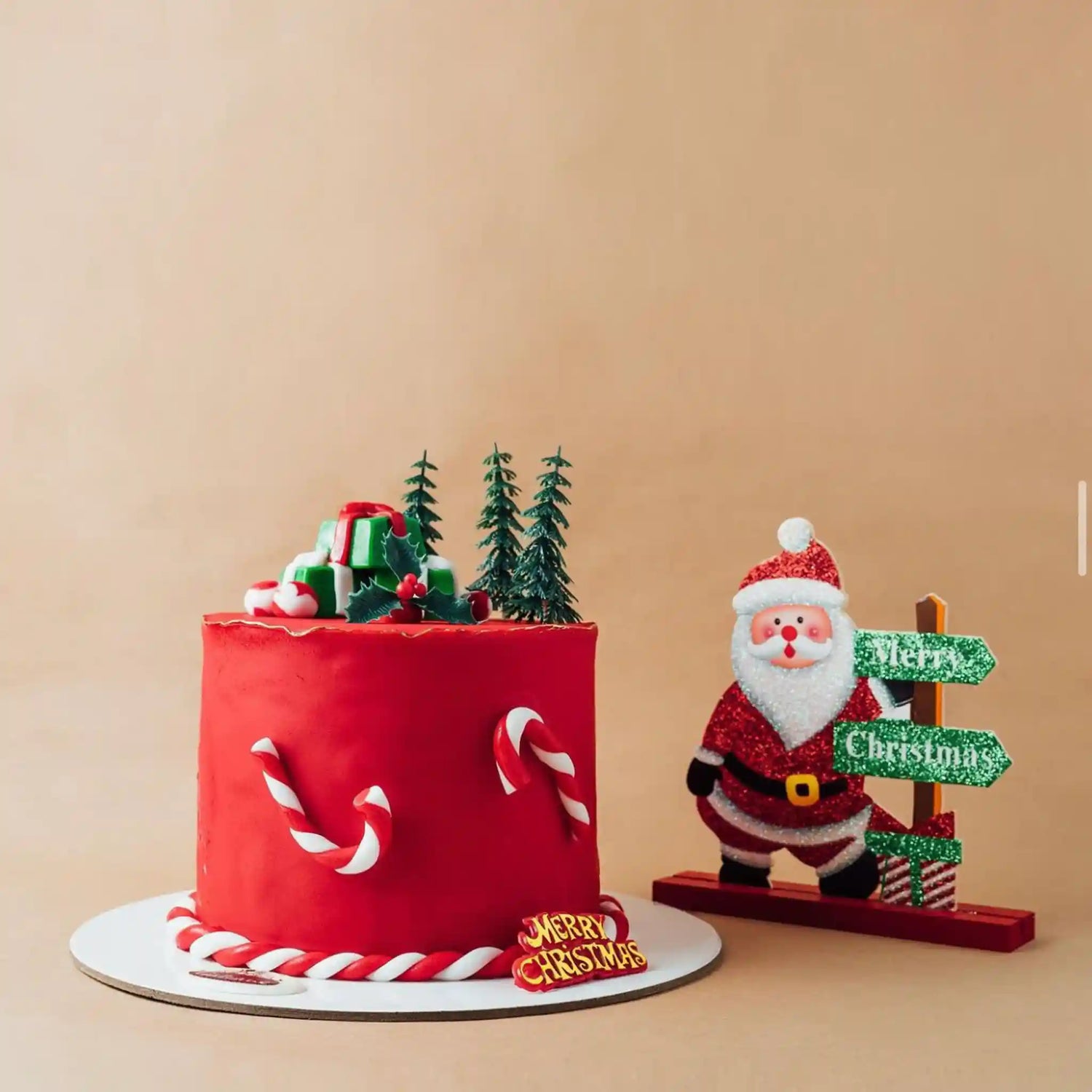 Red Christmas cake with candy cane decorations and a Santa Claus figurine on a beige background