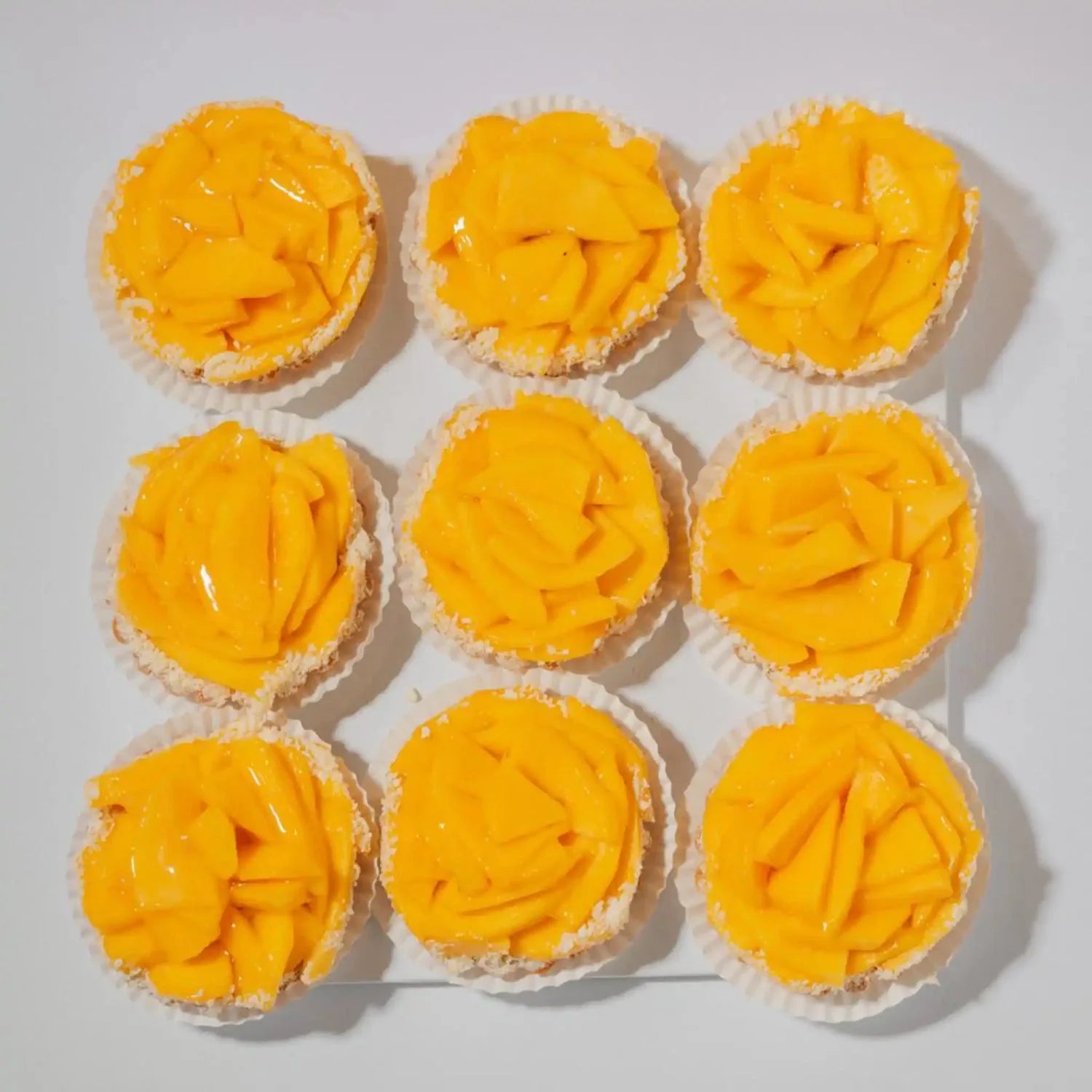 Nine cupcakes with yellow frosting on a white background