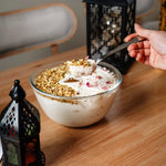 Bowl of dessert with a spoon, on a wooden table with decorative lanterns.
