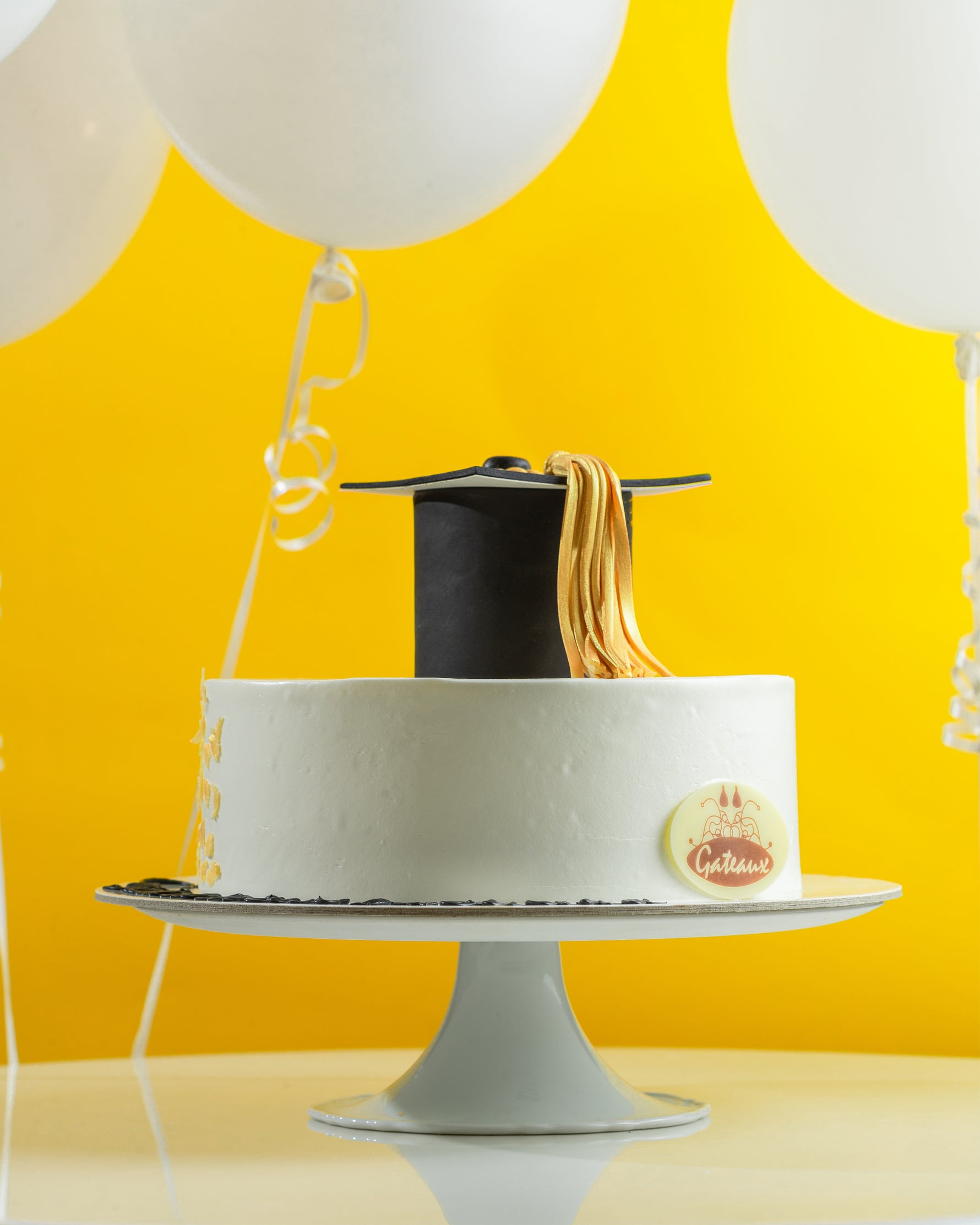 Graduation-themed cake with a black cap and gold tassel on a yellow background