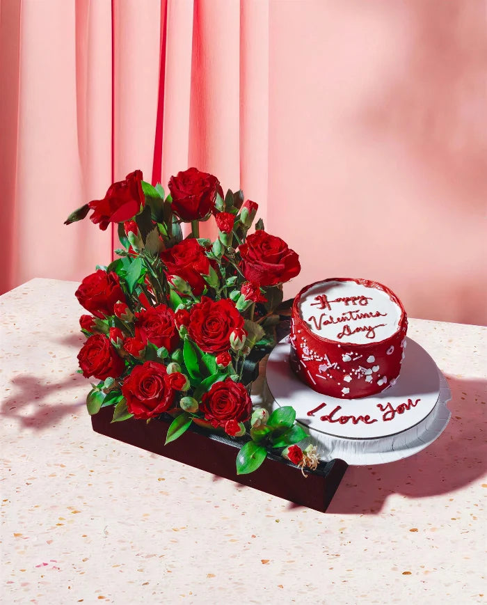 Bouquet of red roses and a red cake with white frosting on a light pink background