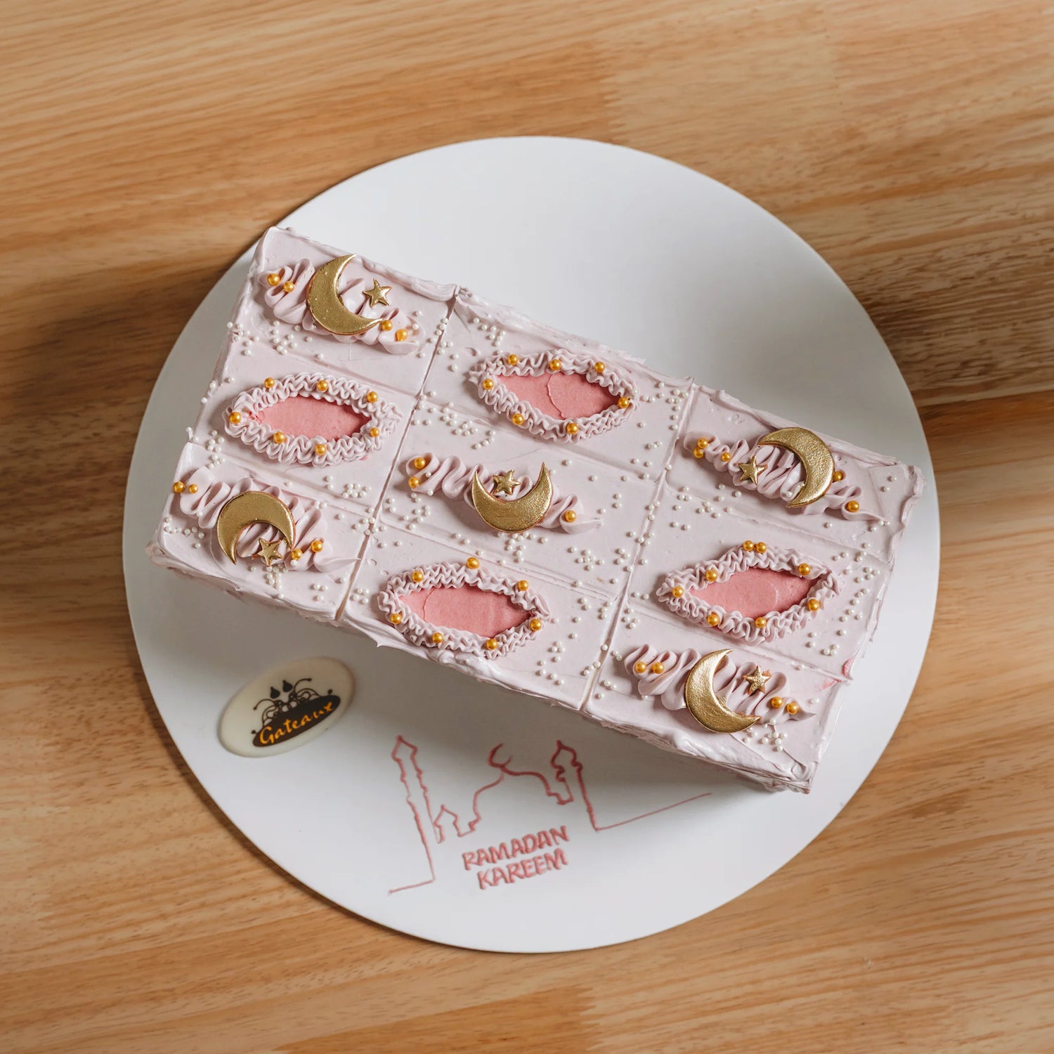 Decorative cake with pink frosting and gold accents on a white plate with 'Ramadan Kareem' text.