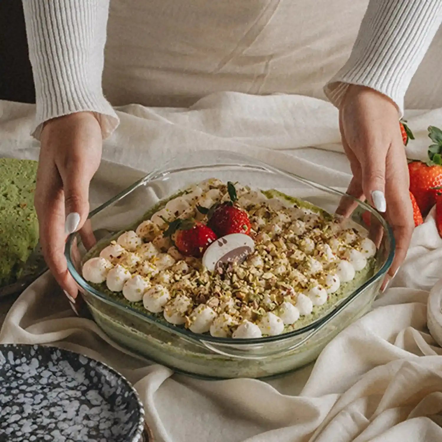 Glass dish with a layered dessert held by two hands on a light fabric background