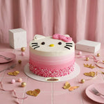 A Hello Kitty themed cake with a pink and white gradient, decorated with a pink bow, black whiskers, and a pink sprinkle border, displayed on a pink table with party decorations.