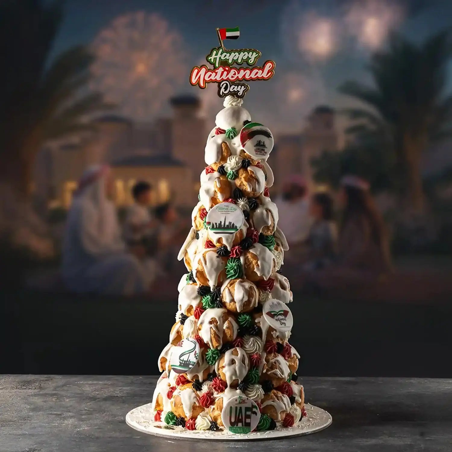 Decorative cake with UAE-themed decorations on a table with a blurred background of people and lights.