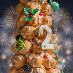 Decorative pastry tower with number '2' and festive decorations against a fireworks background