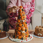 Person decorating a tall, ornate cake with fruit on a table.