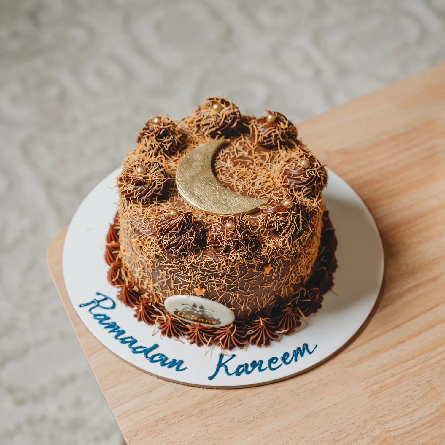 Decorative cake with a gold crescent moon on a 'Ramadan Kareem' plate.
