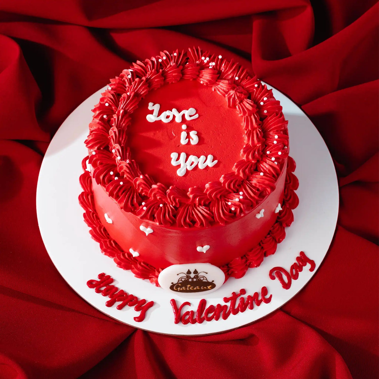 Red Valentine's Day cake with 'Love is you' text on a red fabric background