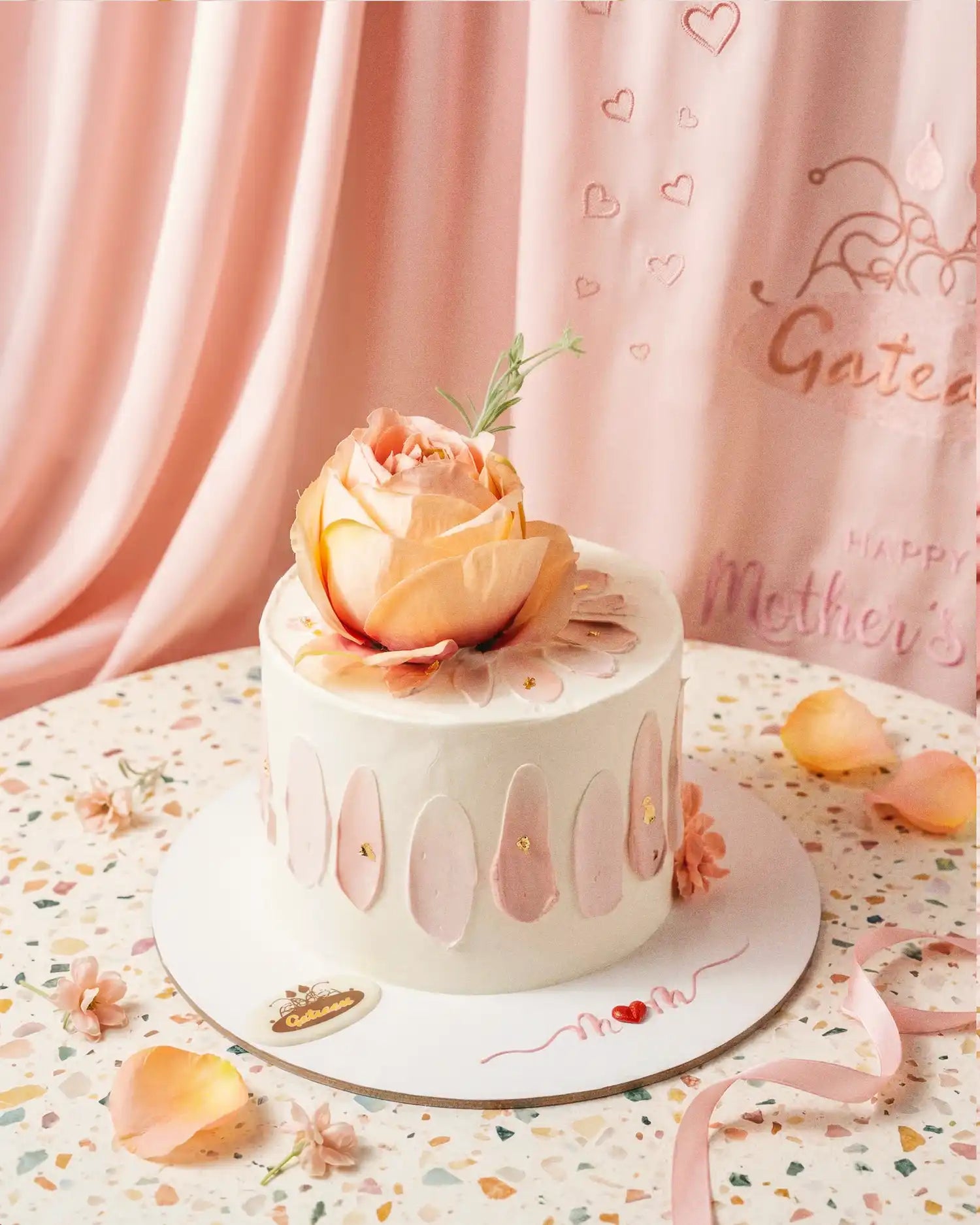 Small white cake with a pink flower on top, placed on a decorative plate with a pink curtain in the background.