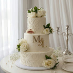 Three-tiered wedding cake with floral decorations and initials 'M' and 'L' on a white background.