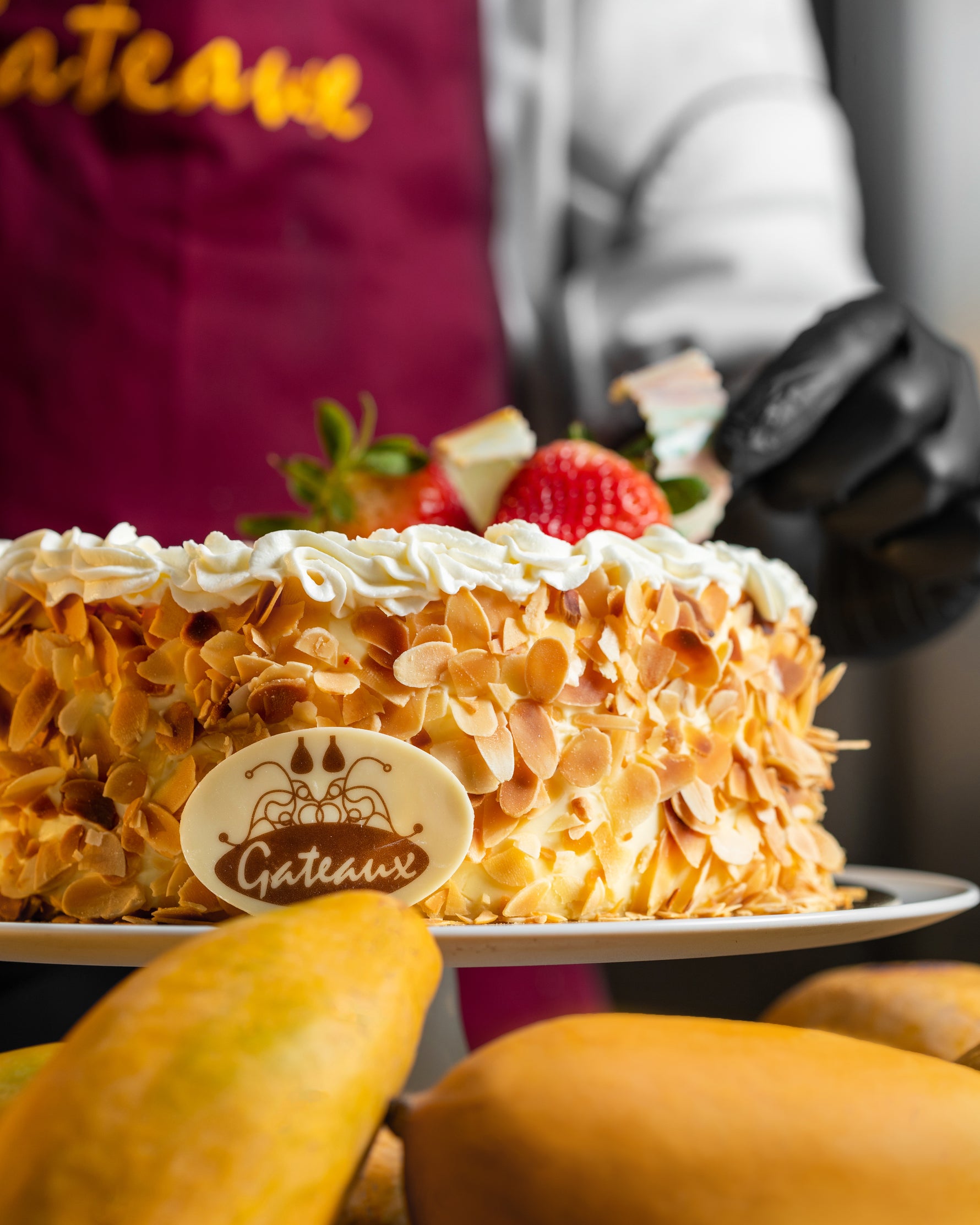 Cake with 'Gâteaux' branding held by a person wearing a maroon apron.
