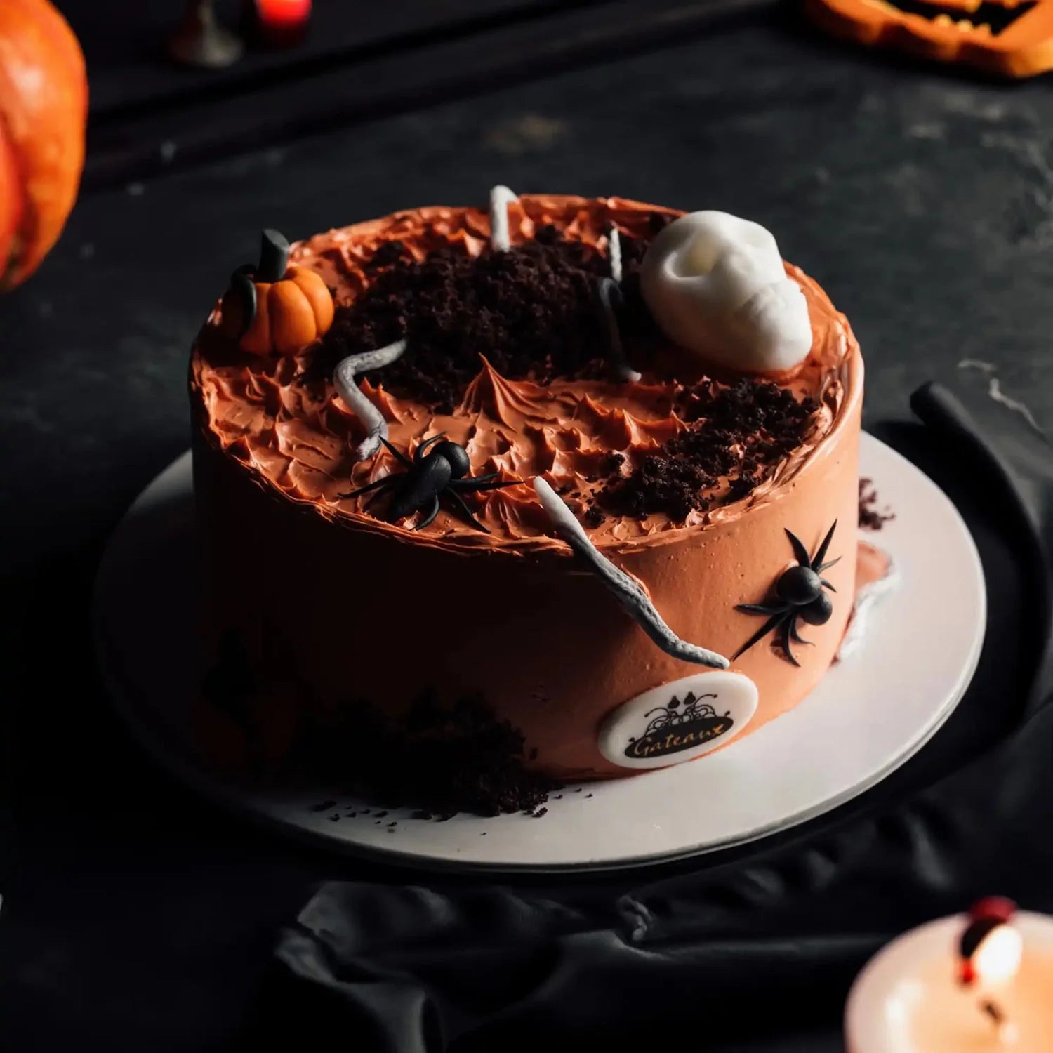 Halloween-themed cake with chocolate frosting, spider decorations, and a skull on a dark background.