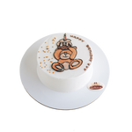 A small round birthday cake with white icing and a decorative bear face and 'Happy Birthday' text on top.