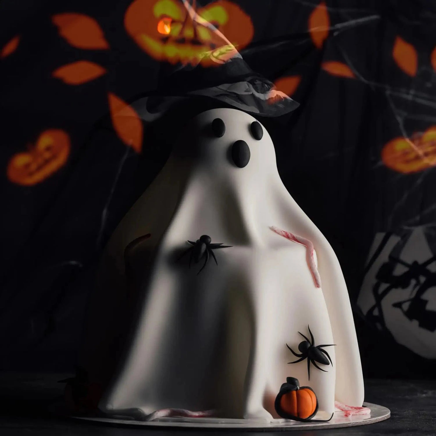 Halloween-themed ghost cake with spiders and pumpkins on a dark background