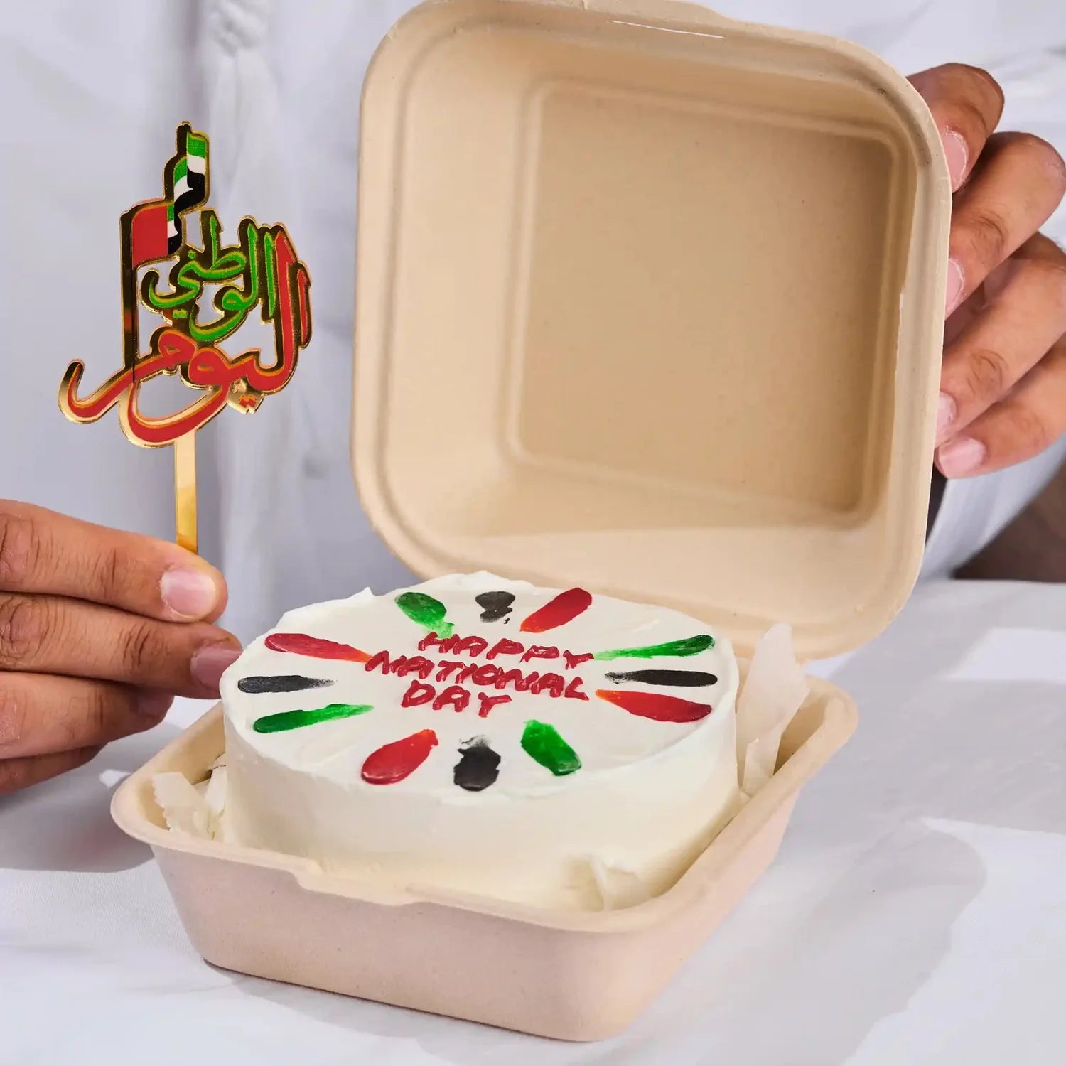 Small cake with 'Happy National Day' text in a takeout container, held by a person.