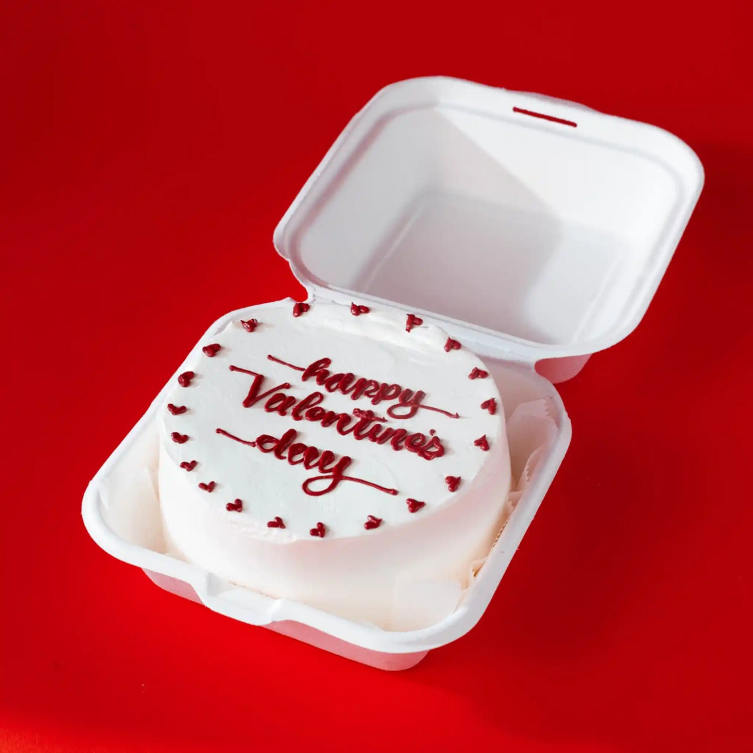 Valentine's Day cake in a takeout container on a red background