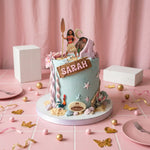 A custom Moana-themed birthday cake with light blue frosting, sand decorations, and character toppers, displayed on a pink table with party props.