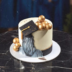 Graduation-themed cake with gold balloons and a black mortarboard on a dark marble surface.