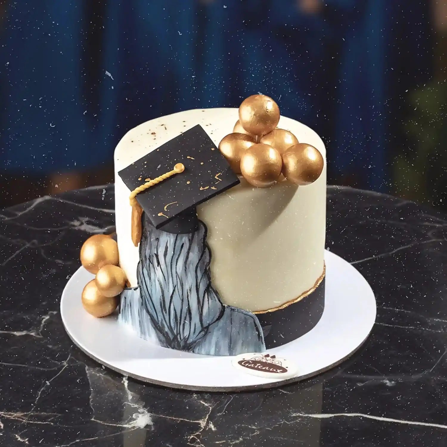 Graduation-themed cake with gold balloons and a black mortarboard on a dark marble surface.