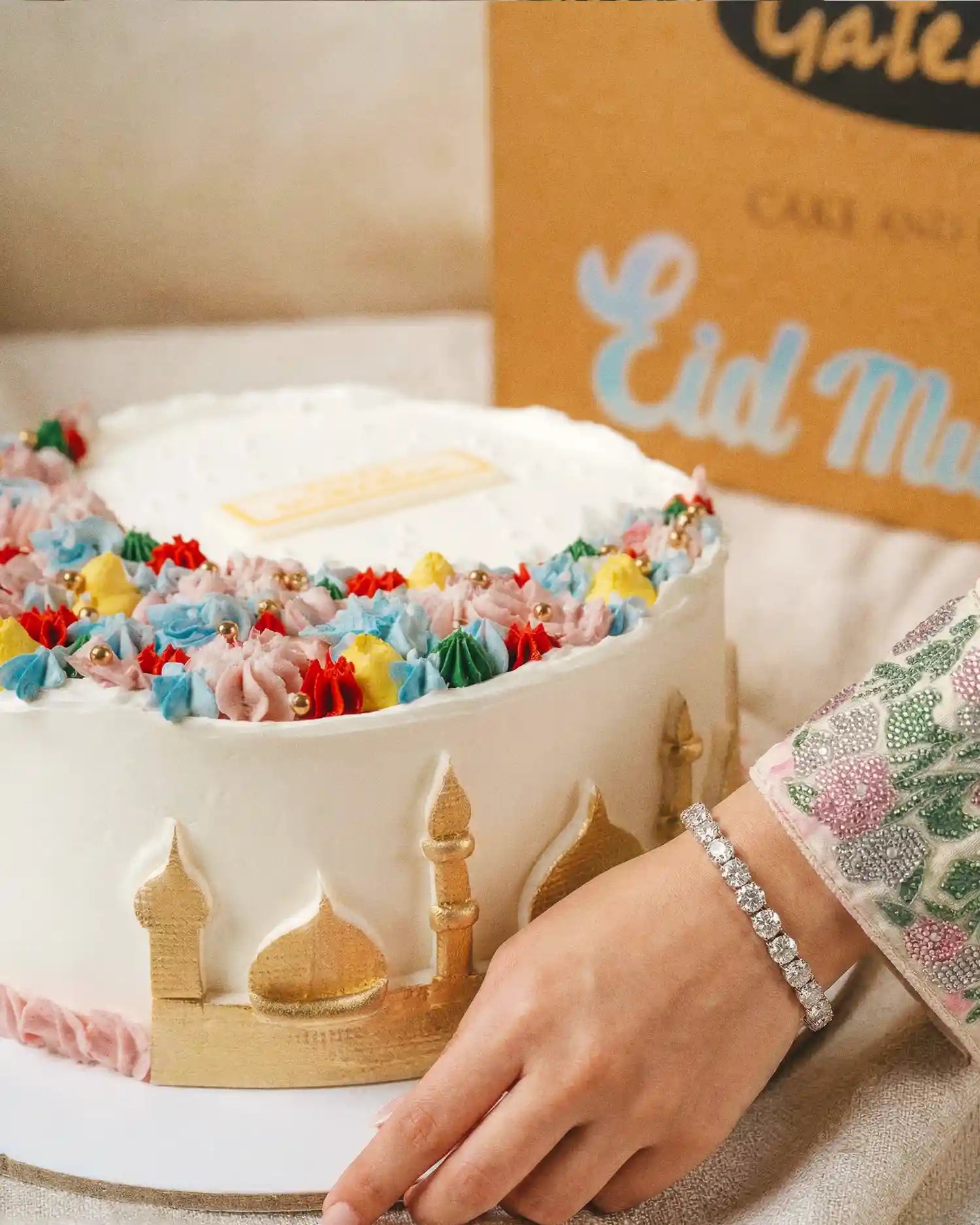 Decorative cake with colorful sprinkles and architectural designs, held by a hand wearing a bracelet.