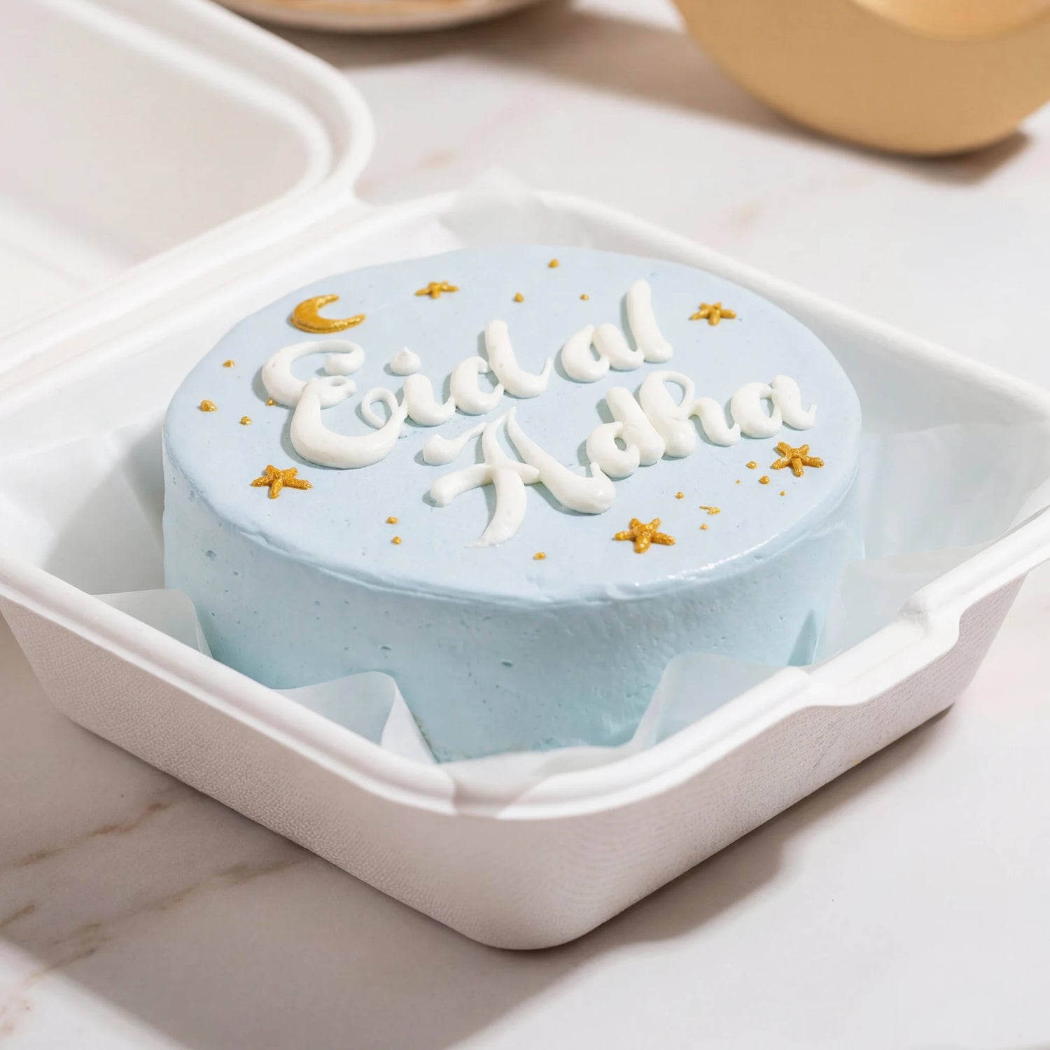 Blue cake with 'Eid al Adha' text in a white container on a marble surface