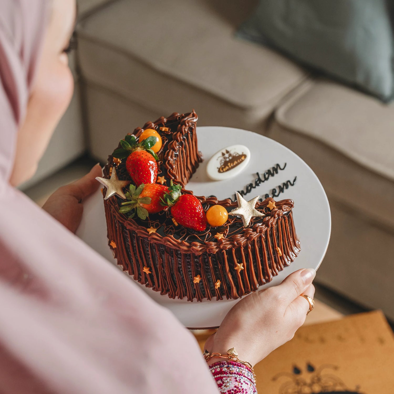 Chocolate cake with fruit decorations on a white plate held by a person.
