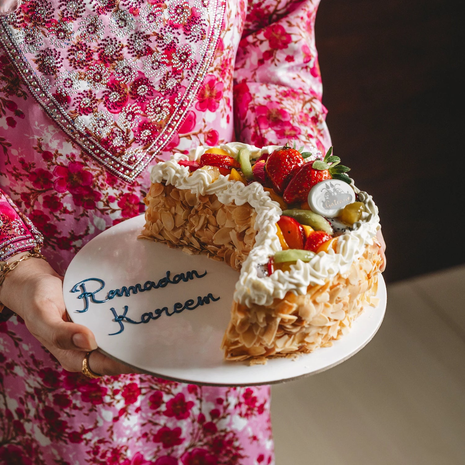 Person holding a slice of decorated cake with 'Ramadan Kareem' on a plate.