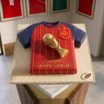 Cake designed like a red and blue sports jersey with a trophy on a marble surface.