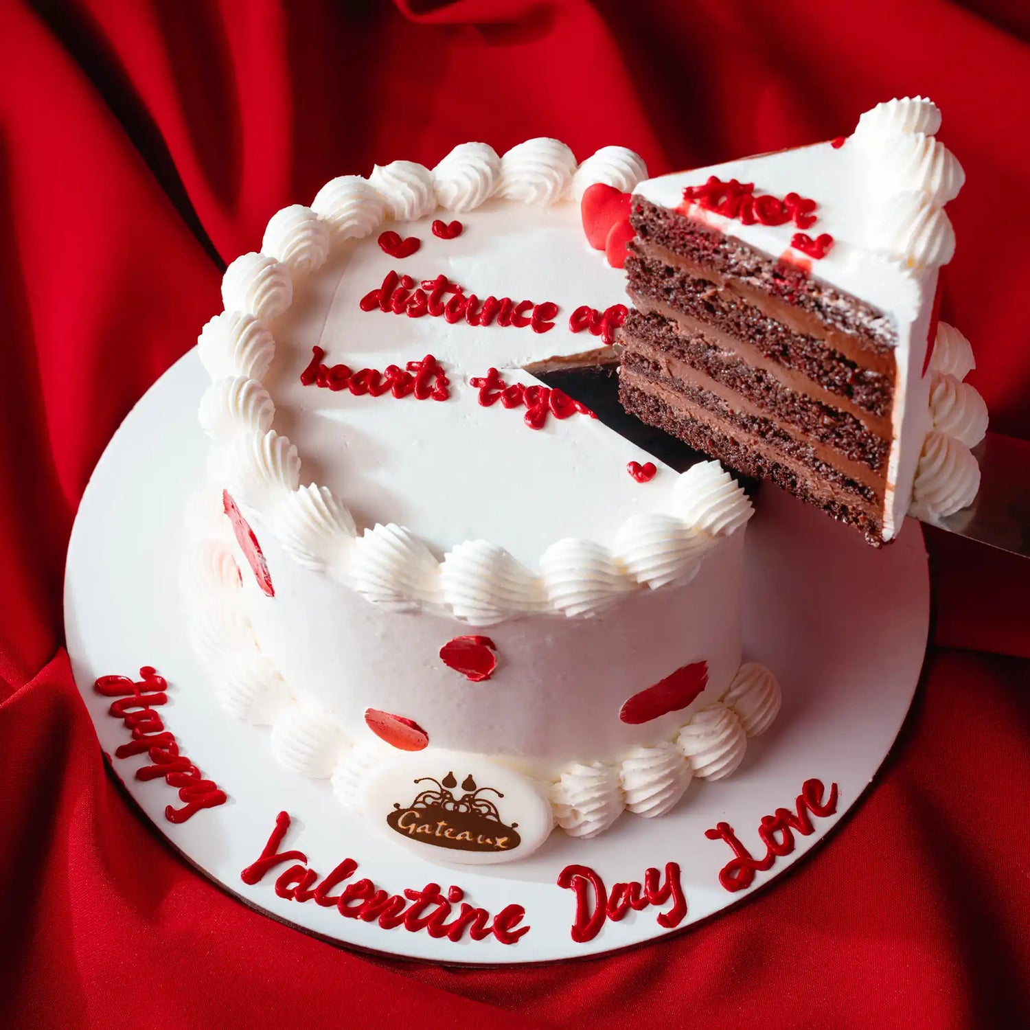 Valentine's Day cake with a slice cut out, red text, and heart decorations on a red background.